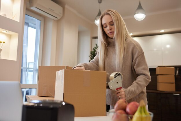 オフィス移転と新しいビジネス コンセプトで段ボール箱をテープで留める若いビジネス女性