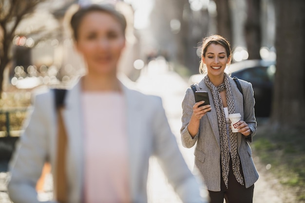 速いコーヒー休憩中に彼女のスマートフォンで入力している若いビジネスウーマン。