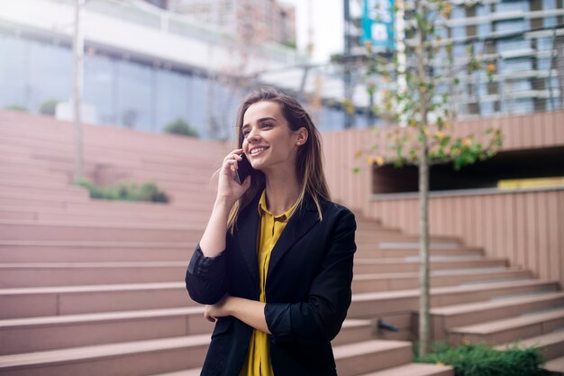 La giovane donna di affari usa il cellulare alla via