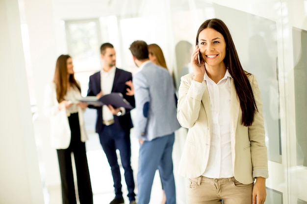 Young business woman uses the phone while other business people talking in the background