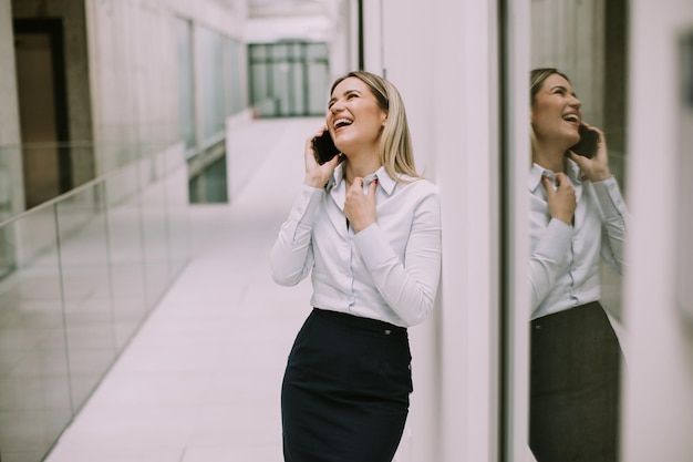 オフィスの廊下で携帯電話を使用する若いビジネス女性