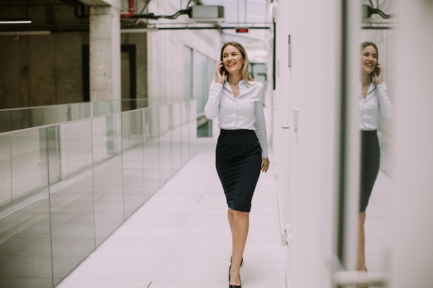 Young business woman using mobile phone in the office hallway