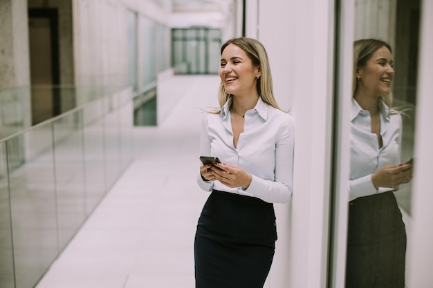 Young business woman using mobile phone in the office hallway