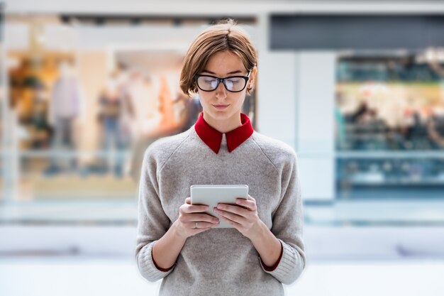 Young business woman using a tablet at a shopping mall. Female person in smart casual clothes in department store working with technology