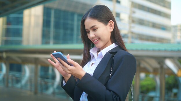 Молодая деловая женщина в черном костюме использует смартфон в городе, концепция делового образа жизни.