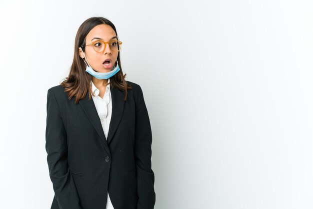 Young business woman wearing a mask to protect from covid isolated on white wall being shocked because of something she has seen