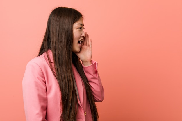 Young business woman wearing pink suit shouting and holding palm near opened mouth