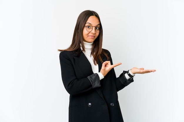 Young business woman on white wall excited holding a blank space on palm.