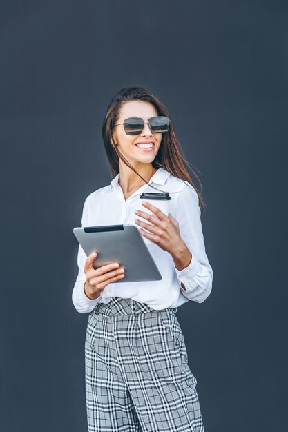 Young business woman with coffee and tablet on grey background.