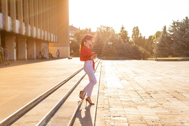 Young business woman with dark hair hurrying up for the meeting walking in the rays of sun