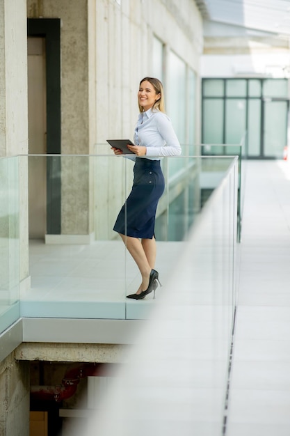 Молодая деловая женщина с цифровым планшетом ходит по стене современного офиса