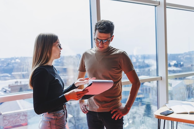 A young business woman with documents in glasses stands with a male manager while holding a corporate business meeting in a modern office Business meeting concept Free space selective focus