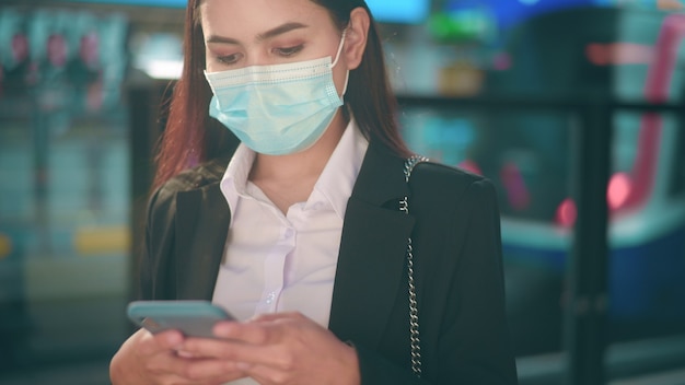 Young business woman with face mask is standing on metro platform using smart.	
