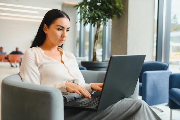 Молодая деловая женщина с ноутбуком сидит в холле бизнес-центра
