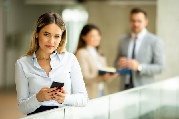 オフィスの廊下で携帯電話を持つ若いビジネス女性