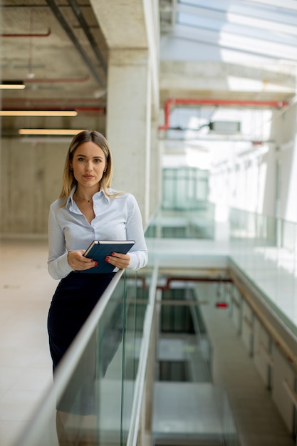 Молодая деловая женщина с ноутбуком, стоящая в стене современного офиса