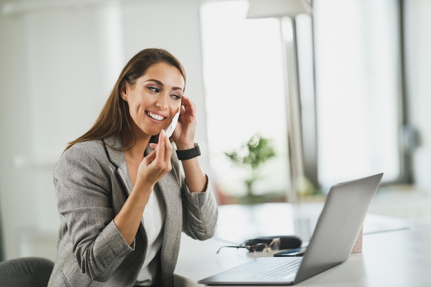 Young business woman with protective mask sitting alone in her home office and working on laptop during COVID-19 pandemic.