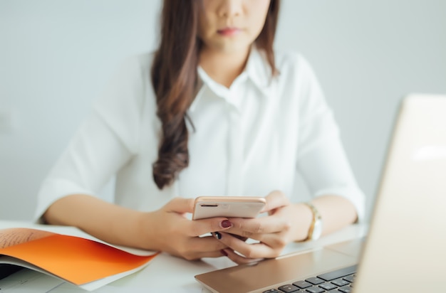 Young business woman working on her smartphone and laptop at workplace.