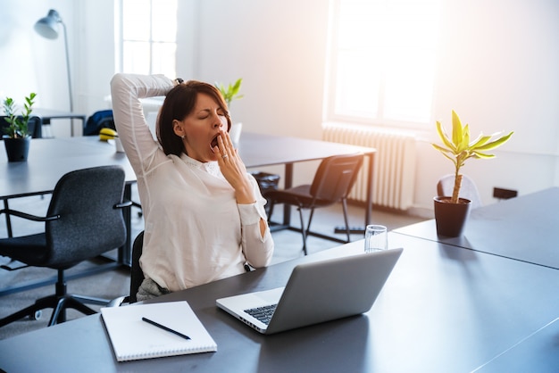 Photo young business woman yawning at a modern office desk in front of laptop