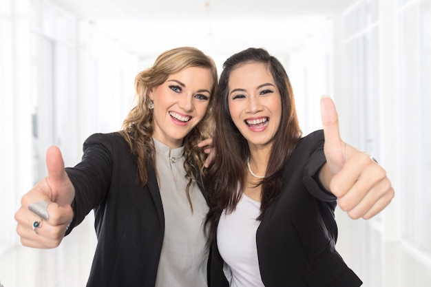 Le giovani donne di affari che fanno i pollici aumentano il gesto che porta la blusa e la giacca