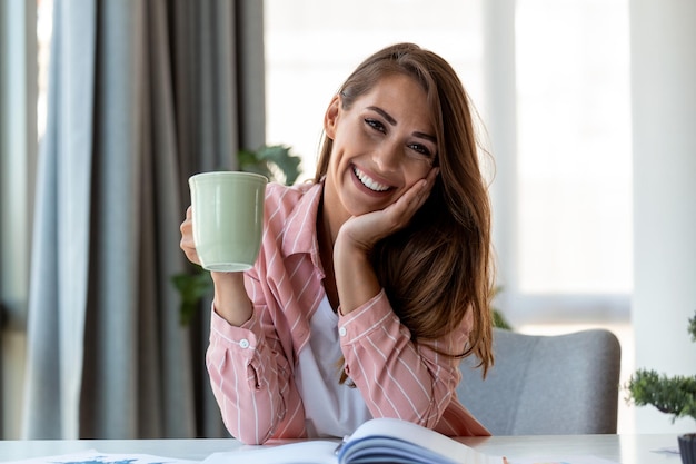 オフィスでコーヒーを飲んでカメラを見ている若いビジネス女性