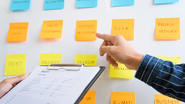 Young business workers posting with sticky notes stickers reminders  creative brainstorming at board the colleague in a modern co-working space.