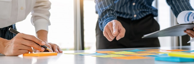 Young business workers posting with sticky notes stickers reminders  creative brainstorming at board the colleague in a modern co-working space.