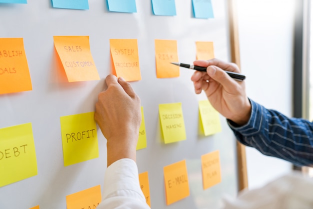 Young business workers posting with sticky notes stickers reminders  creative brainstorming at board the colleague in a modern co-working space.