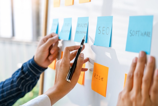 Foto i giovani lavoratori che inviano adesivi appiccicosi ricordano il brainstorming creativo a bordo del collega in un moderno spazio di co-working.