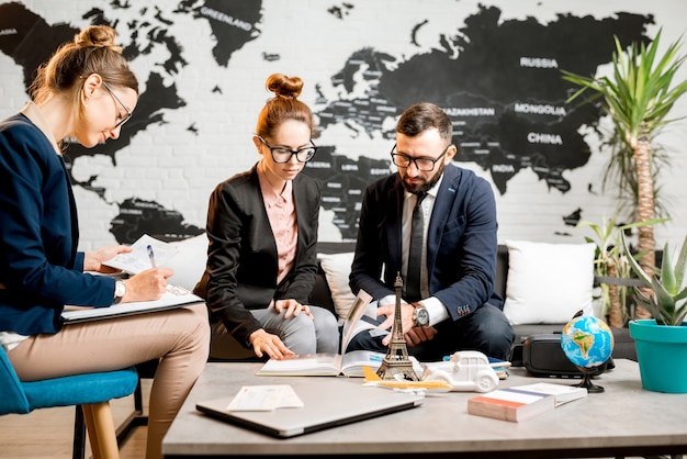 Young businesscouple choosing a trip with agent sitting at the travel agency office with world map on the background