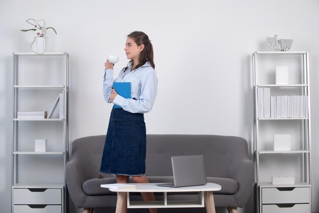 Young businesslady with cup of coffee at workplace in the\
office secretary woman in formal wear working on project at modern\
office