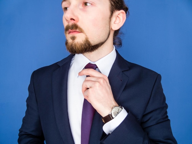 Photo young businessman adjusting tie against blue background