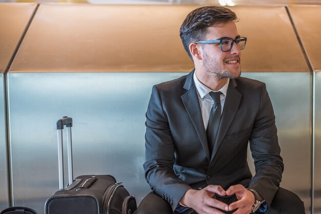 Young businessman at the airport smiling waiting for his flight with luggage