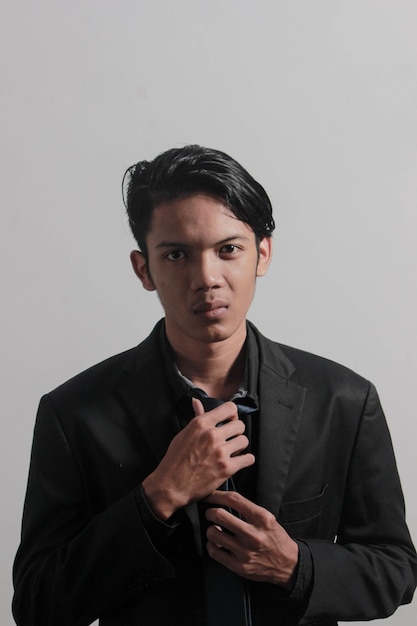 A young businessman in a black shirt, black tie and black suit looks at the camera