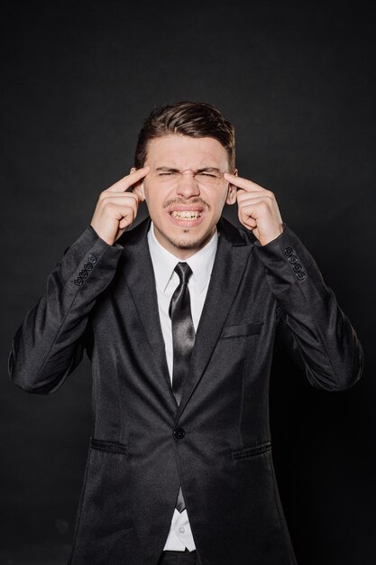 Young businessman in black suit hold hands on head emotions facial expressions feelings body language signs image on a black studio background