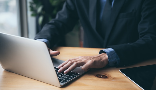 A young businessman in a black suit is working on a laptop from a private residence, working online to reduce the risk of virus infection.