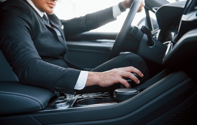 Young businessman in black suit and tie driving modern automobile.