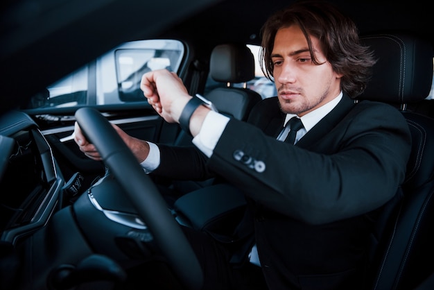 Young businessman in black suit and tie driving modern automobile.