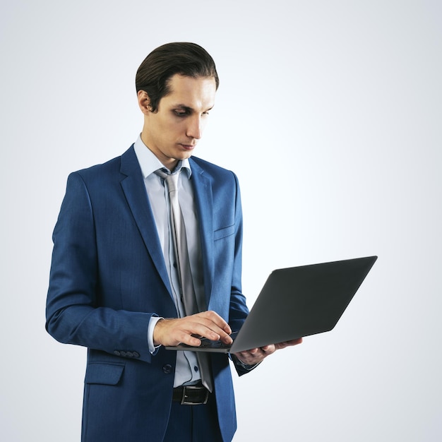 Young businessman in blue suit working with modern laptop isolated on light grey wall background close up