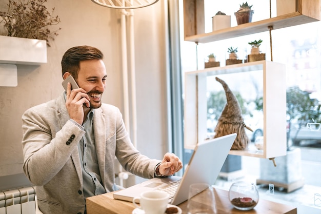 Foto giovane uomo d'affari in pausa in un caffè. sta lavorando al laptop e utilizza lo smartphone.