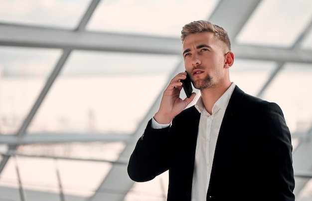 Молодой бизнесмен в бизнес-центре в черном костюме и белой рубашке разговаривает по телефону