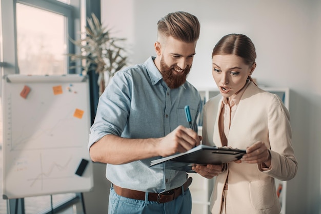 Young businessman and businesswoman discussing new project with clipboard