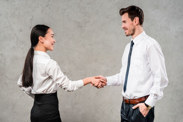 Young businessman and businesswoman shaking each other's hand against grey wall