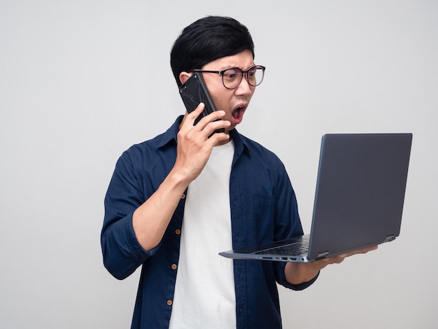 Giovane uomo d'affari impegnato con il telefono cellulare parlante di lavoro e guardando il computer portatile in mano