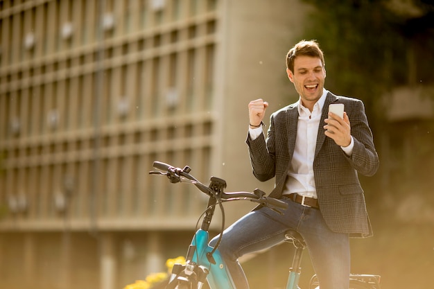 Young businessman on the ebike received gret news by mobile phone