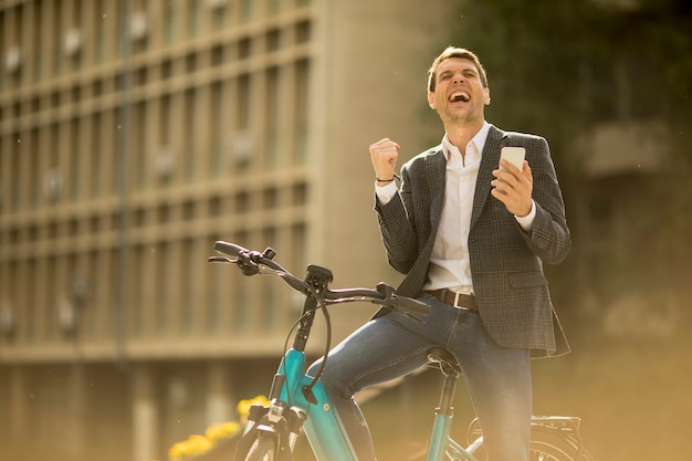 Young businessman on the ebike received gret news by mobile phone