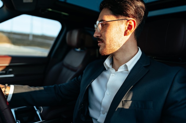 Young businessman in elegant suit driving luxury car