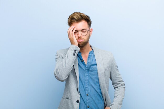 Young businessman feeling bored, frustrated and sleepy after a tiresome, dull and tedious task, holding face with hand