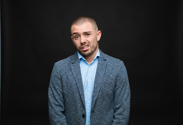 Young businessman feeling puzzled and confused, with a dumb, stunned expression looking at something unexpected against flat wall