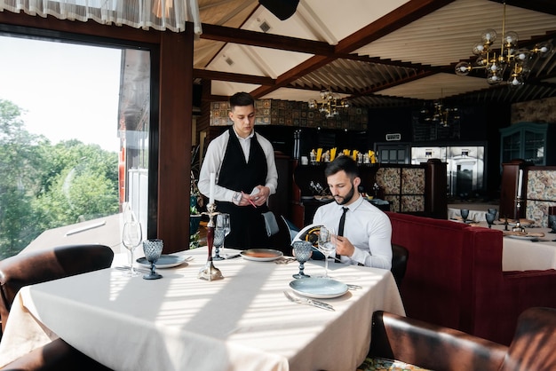 A young businessman in a fine restaurant examines the menu and\
makes an order to a young waiter in a stylish apron customer\
service table service in the restaurant